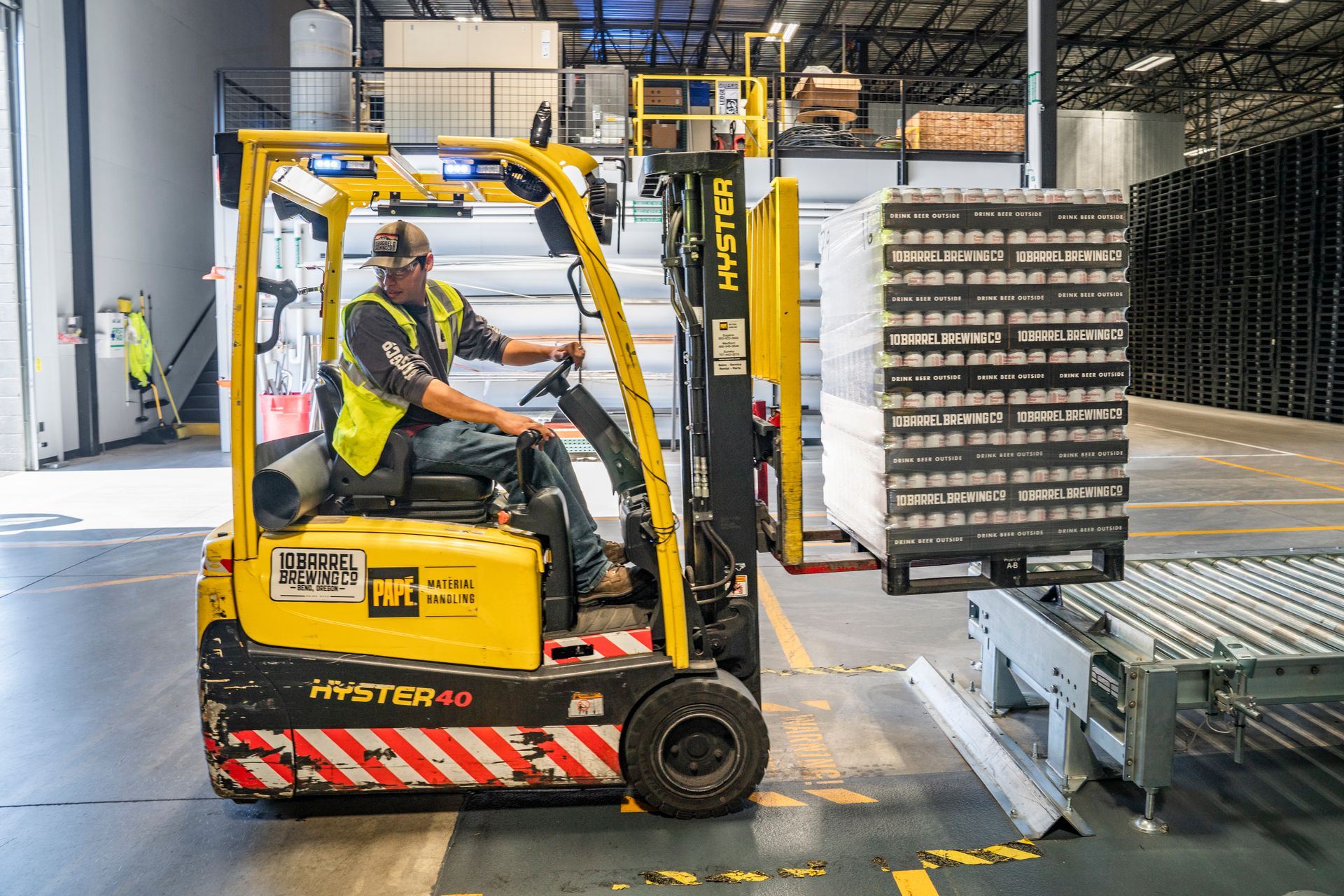 Warehouse worker moving crates with a forklift between tall shelves